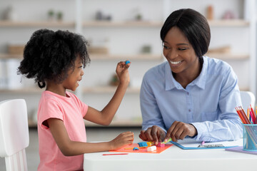 Cute little black girl and teacher playing with play dough