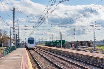 Fototapeta premium Electric passenger train waiting next to the platform, in front of some bulk cargo cars.