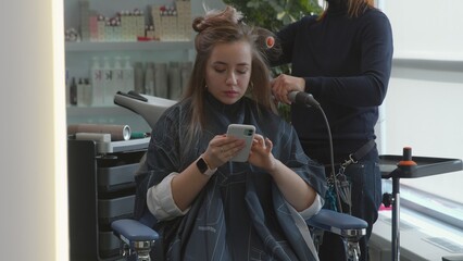A beautiful girl in a hairdressing salon looks at her phone. The girl did her hair. Beauty saloon