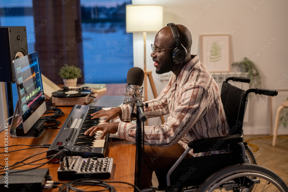 Poster side view of african american musician in wheelchair recording his songs while playing piano keyboar