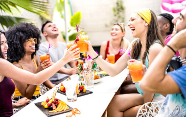 Trendy friends drinking cocktails at poolside party - Young people having fun on luxury resort - Fancy life style concept with guys and girls toasting drinks and fruit together - Bright vivid filter - 492428434