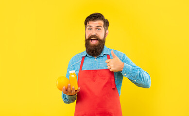 Happy man in apron giving thumb holding orange and juice bottle, juice shopkeeper