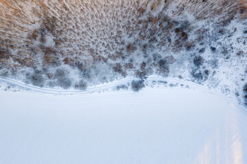 Aerial top down drone view of a road on winter snow covered fields and forest at sunset