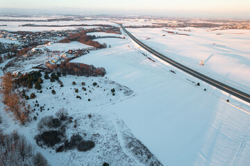 Fototapeta na wymiar Aerial drone view of a highway on winter snow covered fields at sunset