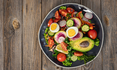 Fototapeta na wymiar Appetizing vegetable salad with eggs, avocado on a wooden background.