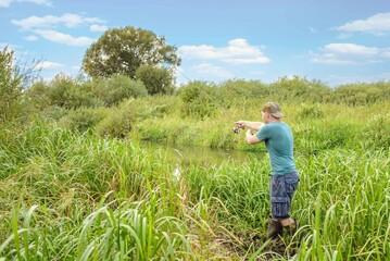 Handsome young man casts a spinning rod on the river bank.