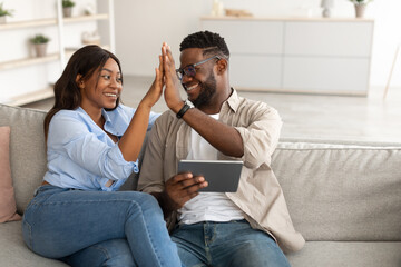 African american couple using tablet, celebrating win giving high five