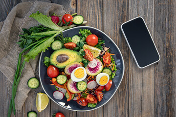 Appetizing vegetable salad with eggs, avocado on a wooden background.