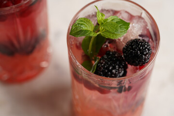 A close up om mint in a long glass with non-alcoholic mocktail version of the classic blackberry and gin cocktail bramble on marble board