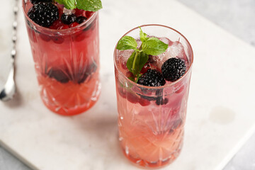 Two long glasses with non-alcoholic mocktail version of the classic blackberry and gin cocktail bramble on marble board