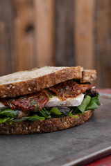 Vegetarian sandwich. Closeup view of a fresh sandwich with arugula, sun dried tomatoes, brie cheese and mushrooms, on the restaurant wooden table. 