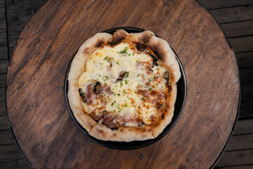 Pizza background. Top view of a pizza with mozzarella cheese, mushrooms, crispy bacon, sliced chives and garlic, on the restaurant wooden table. 
