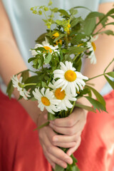 Woman's hands holding bouquet of daisies with orange skirt and blue shirt.