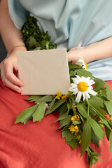 Woman's hands holding blank envelope and daisies with blue shirt and orange skirt closeup.