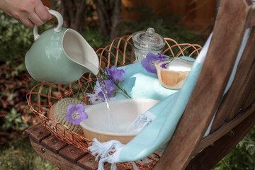 Spa items outdoors in garden in blue and purple colours with hand pouring jug of water into basin. 