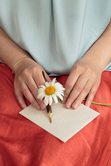 Woman's hands holding daisy flower with pen and blank note paper on orange skirt with blue shirt. 