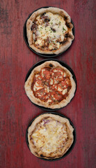 Pizzas. Top view of three pizzas with different ingredients, on the red wooden table. 