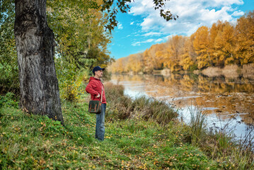 Obraz premium A man with a shoulder bag and a cap walking in a park in summer.