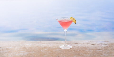 Glass with Cosmopolitan cocktail on the edge of the pool in a resort hotel