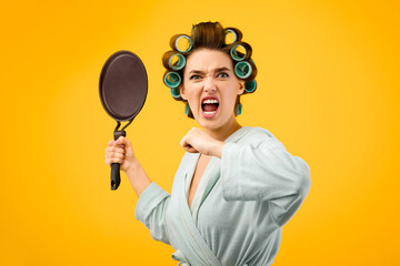 Angry Woman Shouting Holding Frying Pan Over Yellow Studio Background