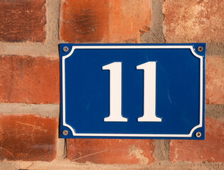 House number eleven on red brick wall | white on blue enamel sign