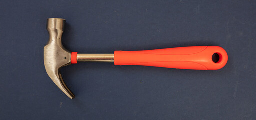 Hammer, steel head, orange color rubber handle on blue background. Overhead, close up view. Banner