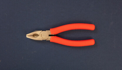 Pliers with steel point, orange color rubber handle on blue background. Overhead, close up view.