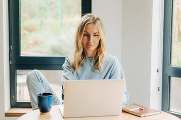 Young blonde woman working sitting on the desk at home office