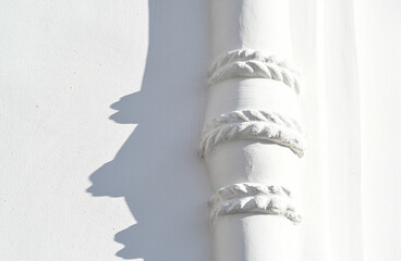 Nice ornament on the wall. Beam with braids. White plastered wall. Illuminated by the sun. Building's facad