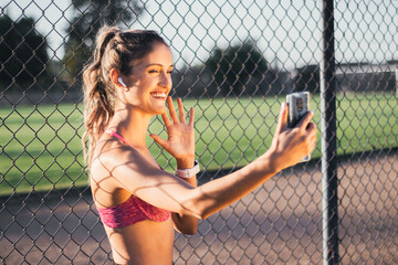 Beautiful and smiling caucasian young active woman making a video call from her mobile, before start running. Earphones