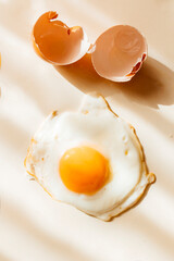 Broken and cracked brown chicken egg and fried egg on pastel yellow background