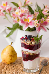 Homemade granola and parfait in tall glasses with yogurt and organic raspberries, nuts and mint. Breakfast on a straw mat with juicy pear, spoon and flowers