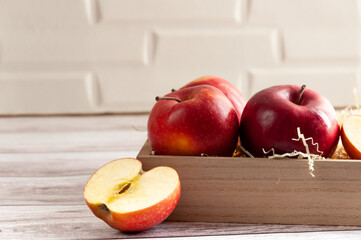 Ripe red apples in wooden box. Simple composition. Box with apple before white wall. The half of apple. Space for your text. Selective focus.
