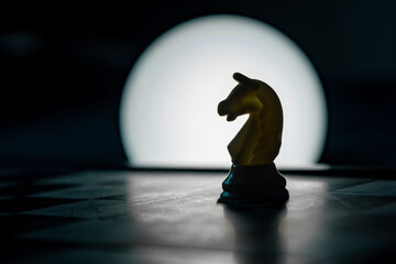 A chess piece - a knight stands on a chessboard, with reverse illumination. A strategic game of...