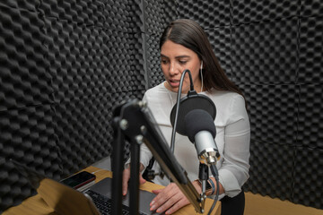 Obraz na płótnie Canvas Woman speaking into a microphone in an audio booth, while recording a podcast