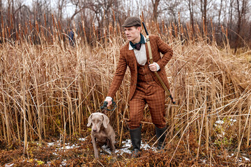 attentive gray hunter dog leads owner man to the side, directs. in countryside nature, rural place. confident male with rifle following the dog, professionally equipped. hunting as hobby.