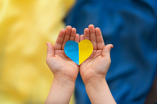 
A heart-shaped badge depicting the State Flag of Ukraine as a symbol of patriotism and pride in one's country. State symbol of Ukraine in children's hands against the background of the Ukrainian flag