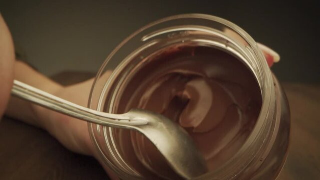 Chocolate paste in a jar. Close-up of a spoonful of chocolate cream in a glass jar on a dark background.