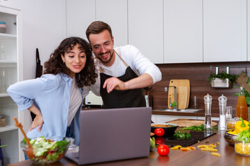Happy couple using laptop computer preparing healthy food diet vegetable salad at home together....