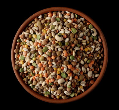 Mixed legumes and cereals, peeled barley, green, yellow and dark red lentils, half green peas, black white beans, green beans in clay pot isolated on black background, top view