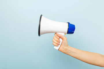 Womans hand is holding a megaphone on blue background. Concept of speech and announce, idea for marketing or sales