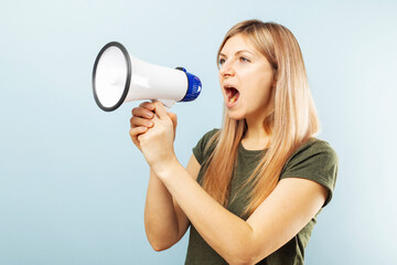 Young blonde woman shouting loudly while holding a megaphone on blue background. Concept of speech and announce, idea for marketing or sales