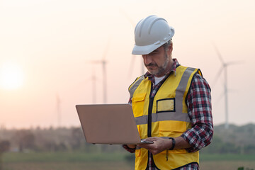 Portrait of power engineer wearing safety jacket and hardhat with laptop computer working at...