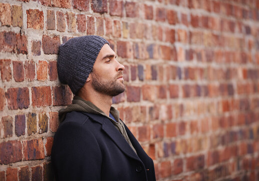 City style. Cropped shot of a fashionable man leaning against a brick wall in an urban setting.