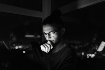 Black and white dark portrait of young man looking in smartphone.