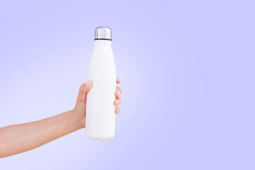 Hand holding white steel bottle on background of very peri color. Close-up view.