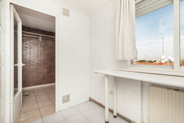 White countertop with two legs below a window with views and access to a terrace with stoneware floors and a dark brown brick wall