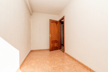 empty room with orange stoneware floor, mahogany wood door and white painted walls and brass door handle