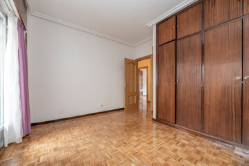 empty room with oak parquet floor, white painted walls and aluminum window with curtains and net curtains and built-in wardrobe with wooden doors