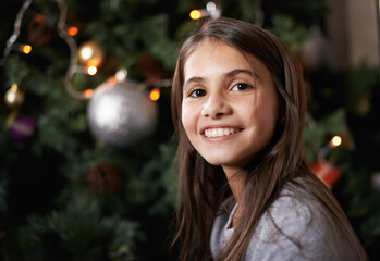 Its a joyful time of year. Shot of a little girl sitting by a christmas tree.